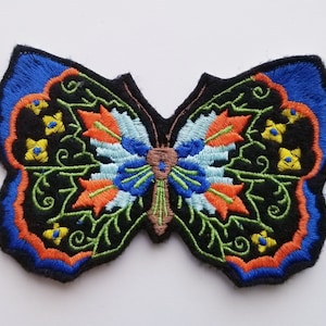 May include: A black felt embroidered butterfly patch with blue, orange, green, and yellow details. The butterfly has a detailed design with intricate floral patterns.
