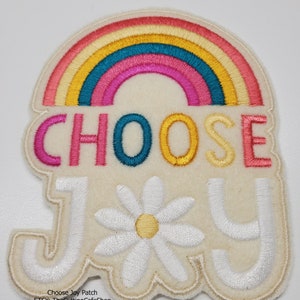 May include: White felt patch with a rainbow, the words "CHOOSE JOY" and a white daisy. The rainbow is made of pink, red, orange, yellow, teal, and light blue.