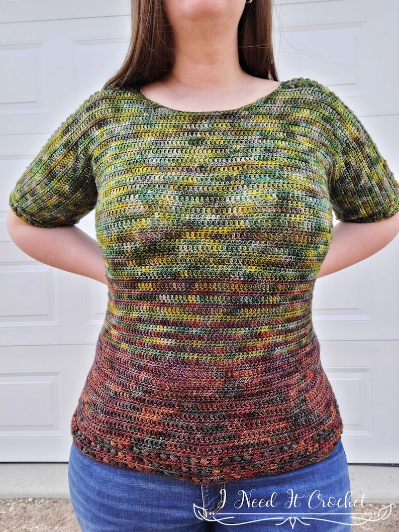May include: A crochet top with a striped pattern in shades of green, brown, and orange. The top has a scoop neck and short sleeves. The bottom of the top has a crocheted border.