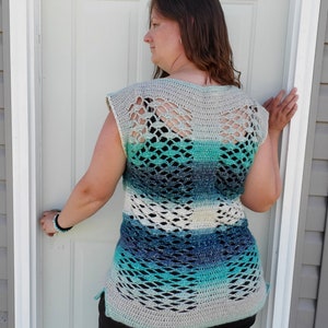 May include: A crocheted top with a blue, green and white ombre design. The top has a wide, open neckline and a loose, flowing fit. The back of the top features a delicate, openwork pattern.