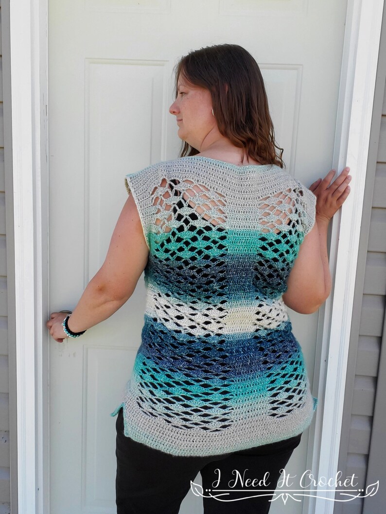 May include: A crocheted top with a blue, green and white ombre design. The top has a wide, open neckline and a loose, flowing fit. The back of the top features a delicate, openwork pattern.
