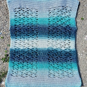 May include: A crocheted blanket with a lacy pattern in shades of blue and grey. The blanket is made with a gradient yarn that transitions from light grey to dark blue.