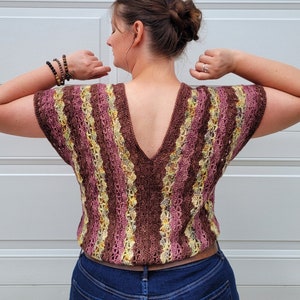 May include: A brown, pink, and yellow striped crochet top with a deep V-neck back. The top is worn with blue jeans.