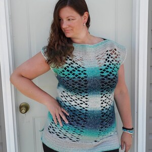 May include: A crocheted top with a blue, green and white ombre pattern. The top has a loose fit and a wide neckline. It features a delicate openwork design throughout.