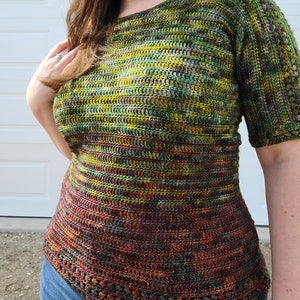 May include: A crochet top with a green, yellow, and brown color scheme. The top has a scoop neck and short sleeves. The bottom of the top has a crocheted border.