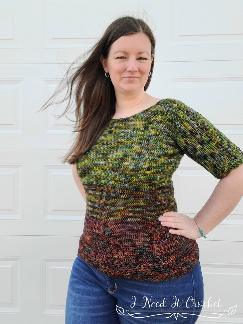 May include: A green, brown, and orange crochet top with a loose fit and short sleeves. The top has a gradient pattern and is worn with blue jeans.