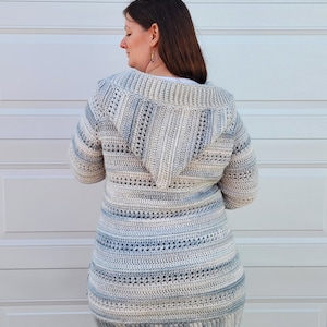 May include: A hooded cardigan with a striped pattern in shades of blue and beige. The cardigan is crocheted and has a long, loose fit.