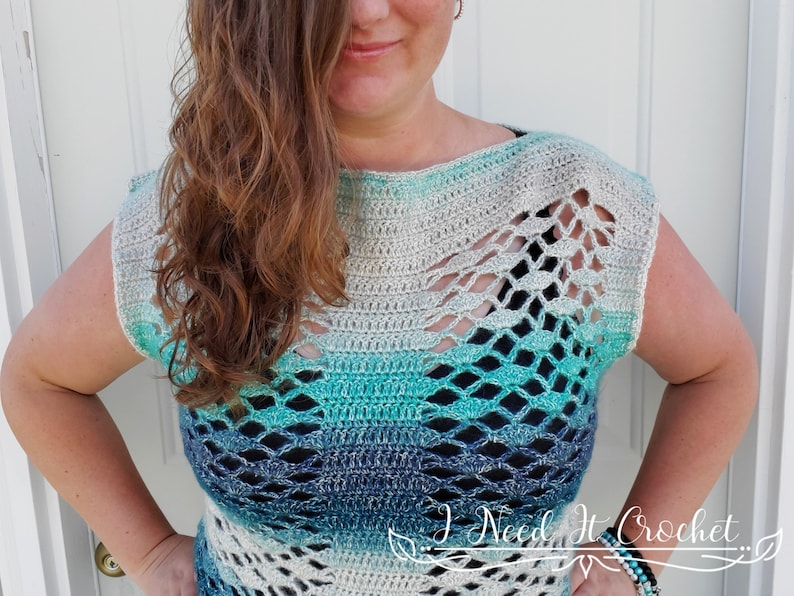 May include: A crocheted top with a light blue, teal and white ombre design. The top has a loose fit and a wide neckline. It features a delicate openwork pattern throughout.