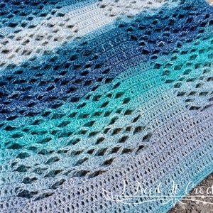 May include: A crocheted shawl with a gradient of blue and green colours. The shawl has a lacy pattern and is made with a soft yarn.