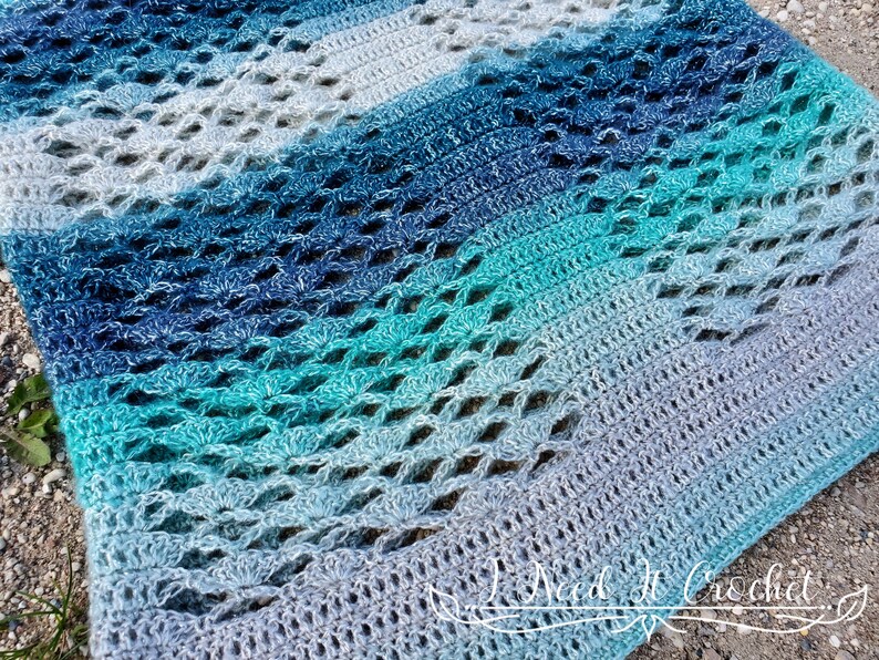 May include: A crocheted shawl with a gradient of blue and green colours. The shawl has a lacy pattern and is made with a soft yarn.
