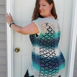May include: A crocheted top with a blue, green and white ombre design. The top has a wide, open neckline and a loose, flowing fit. The back of the top features a delicate, openwork pattern.