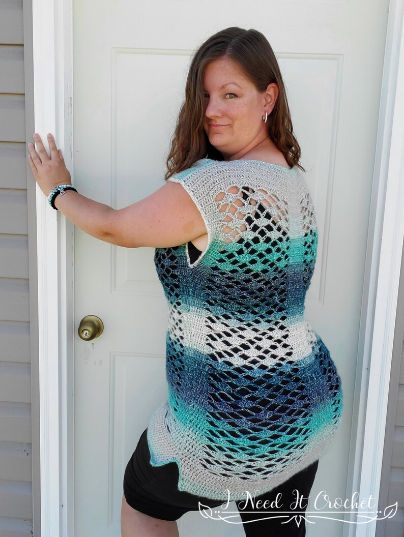 May include: A crocheted top with a blue, green and white ombre design. The top has a wide, open neckline and a loose, flowing fit. The back of the top features a delicate, openwork pattern.