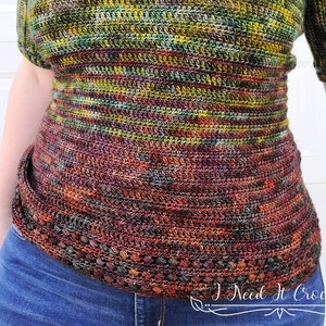May include: A close-up of a crocheted top with a colorful, variegated yarn in shades of green, brown, and orange. The top has a fitted bodice and a wide, flared hem. The text "I Need It Crochet" is visible in the lower right corner of the image.