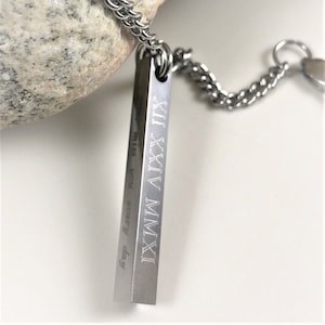 May include: A silver-colored pendant necklace with a rectangular bar. The bar is engraved with Roman numerals and the words "every day" and "miss". The necklace chain is also silver-colored.