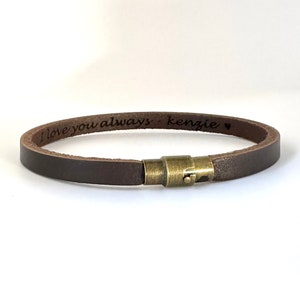 Peut inclure: Un bracelet en cuir marron avec une fermeture en laiton. Le bracelet est gravé avec le texte "I love you always - kenzie" et un symbole de cœur.