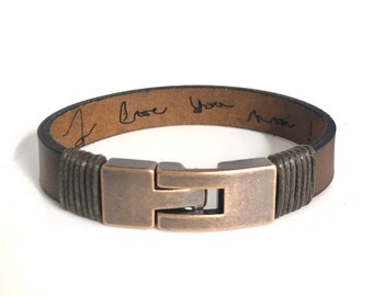 May include: A brown leather bracelet with a silver clasp. The inside of the bracelet is engraved with the words "I love you mom!"