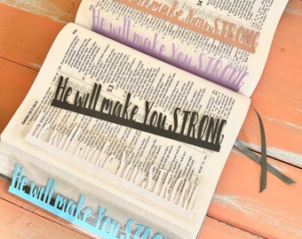 Puede incluir: Primer plano de una Biblia con varios marcadores que dicen "Él te hará fuerte". Los marcadores son de diferentes colores, incluyendo negro, azul, morado y rosa.