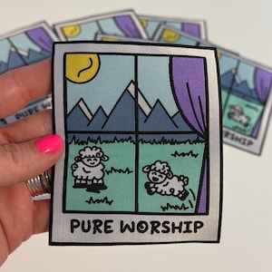 May include: A white iron-on patch with a cartoon window scene. The window shows a blue sky with a yellow sun, mountains, and two white sheep. The text "PURE WORSHIP" is printed below the window.