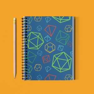 Può includere: Un quaderno a spirale blu con un motivo di forme geometriche colorate. Il quaderno è su una superficie gialla con una matita accanto.