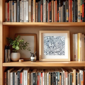 May include: A black and white illustration of a fox curled up in a nest of leaves. The illustration is framed and hanging on a bookshelf with books on either side.