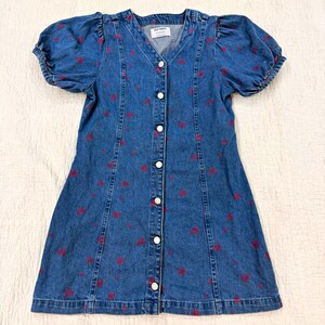 May include: A blue denim dress featuring a V-neckline, short puff sleeves, and a front button-down closure. The fabric is patterned with small red heart shapes throughout. An Old Navy brand label is visible at the inner neckline of the garment.