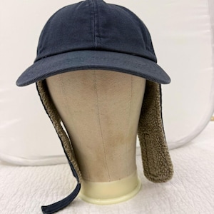 May include: A dark navy blue baseball cap featuring a structured crown and a curved brim. The cap includes integrated ear flaps lined with a textured, tan-colored fleece material that extends downward from the sides of the cap for coverage.
