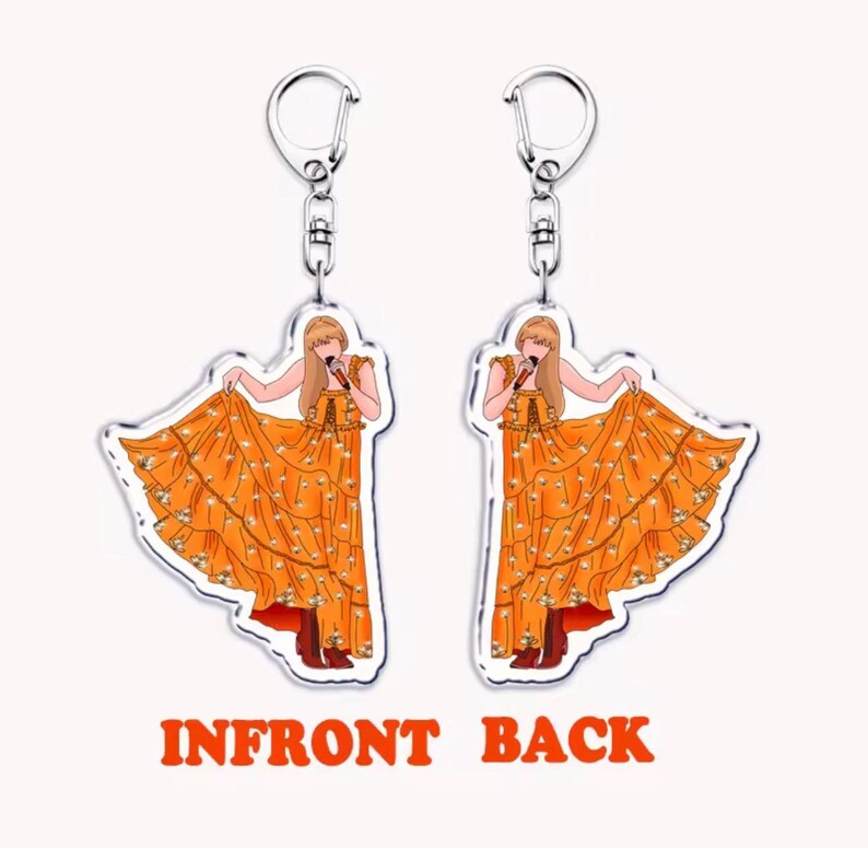 May include: Two clear acrylic keychains with a cartoon illustration of a person in an orange dress holding a microphone. The dress has white floral accents. The keychains have silver-coloured metal hardware. The text "INFRONT BACK" is in orange.