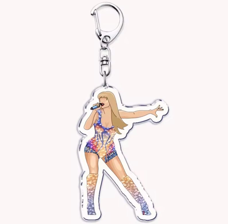 May include: A clear acrylic keyring featuring a stylized illustration of a female singer in a colorful bodysuit and boots, holding a microphone. The keyring has a silver-coloured metal clasp.