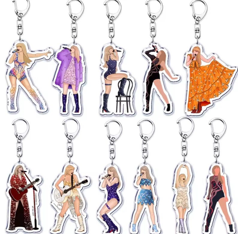 May include: A selection of clear acrylic keyrings, each displaying a different illustration of a singer in performance attire. The keyrings have silver-coloured metal rings and clasps for attaching to keys or bags. The illustrations depict the singer with a microphone.