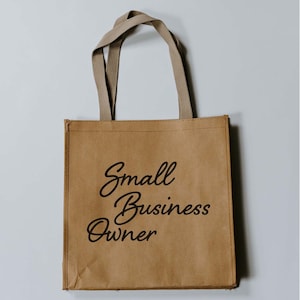 Può includere: Una borsa di tela di carta marrone con manici beige. La borsa ha il testo "Small Business Owner" stampato in nero.