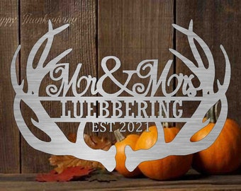 May include: A silver metal sign with the words "Mr & Mrs" above the last name "LUEBBERING" and "EST 2021" within a decorative antler design. Pumpkins and fall leaves are in the background.