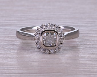 Könnte beinhalten: Ein silberner Ring mit einem quadratischen Diamanten, der in einem Halo aus kleineren Diamanten gefasst ist.