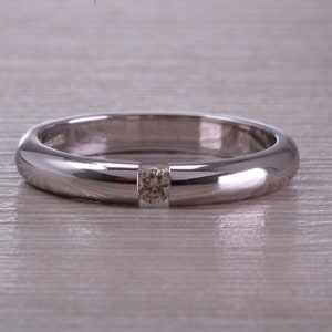Puede incluir: Una banda de plata simple con un solo diamante redondo pequeño engastado en el centro.