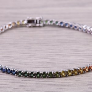 May include: A rainbow sapphire tennis bracelet with a silver clasp. The bracelet is made of small, round sapphires set in silver.