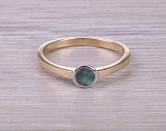 May include: A gold ring with a round, green gemstone set in a silver bezel. The ring has a simple, elegant design, perfect for everyday wear. The band is a polished gold color.