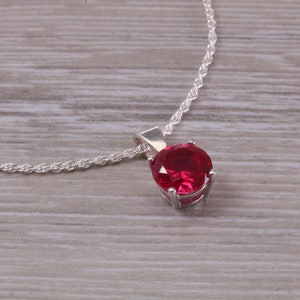 May include: A silver chain necklace with a red gemstone pendant.