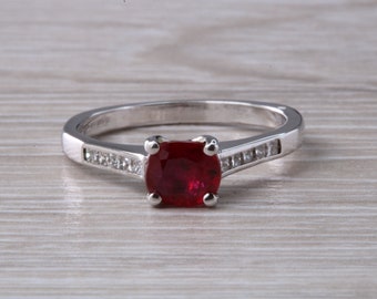 Puede incluir: Un anillo de plata con una piedra preciosa roja y una fila de piedras preciosas transparentes más pequeñas a cada lado.