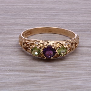 May include: A gold ring with a purple amethyst gemstone and two green peridot gemstones set in a delicate filigree design.