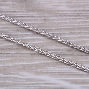 Puede incluir: Un collar de cadena de plata con un diseño trenzado.