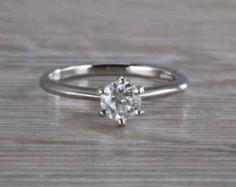 May include: A simple silver solitaire engagement ring with a single round diamond.