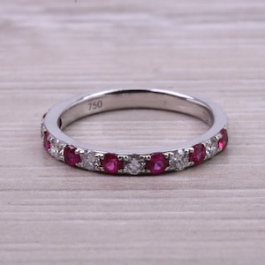 May include: A white gold band ring with a row of alternating ruby and diamond stones. The ring is marked "750" on the inside.