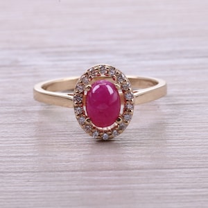 May include: A gold ring with a large oval-shaped ruby gemstone surrounded by a halo of smaller diamonds.