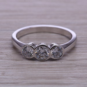 Puede incluir: Un anillo de plata con tres piedras preciosas redondas y transparentes engastadas en fila.