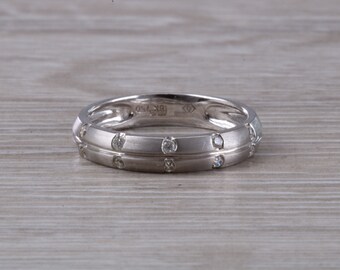 May include: A silver wedding band with a row of small diamonds set into the band. The band has a slightly rounded profile and a polished finish.