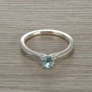May include: A silver ring with a light blue gemstone set in the centre.