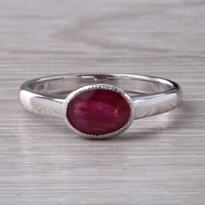 May include: A silver ring with a bezel setting featuring a deep red oval ruby.