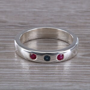 May include: A silver band ring with three gemstones. Two red gemstones and one blue gemstone are set in the band.