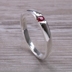 Op de afbeelding: Een zilveren ring met een enkele rode edelsteen in het midden.