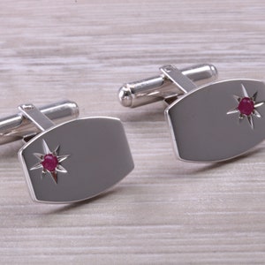 May include: A pair of silver cufflinks featuring a star design with a red gemstone at the centre of each star.