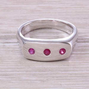 May include: A silver ring with three pink gemstones set in a rectangular shape.